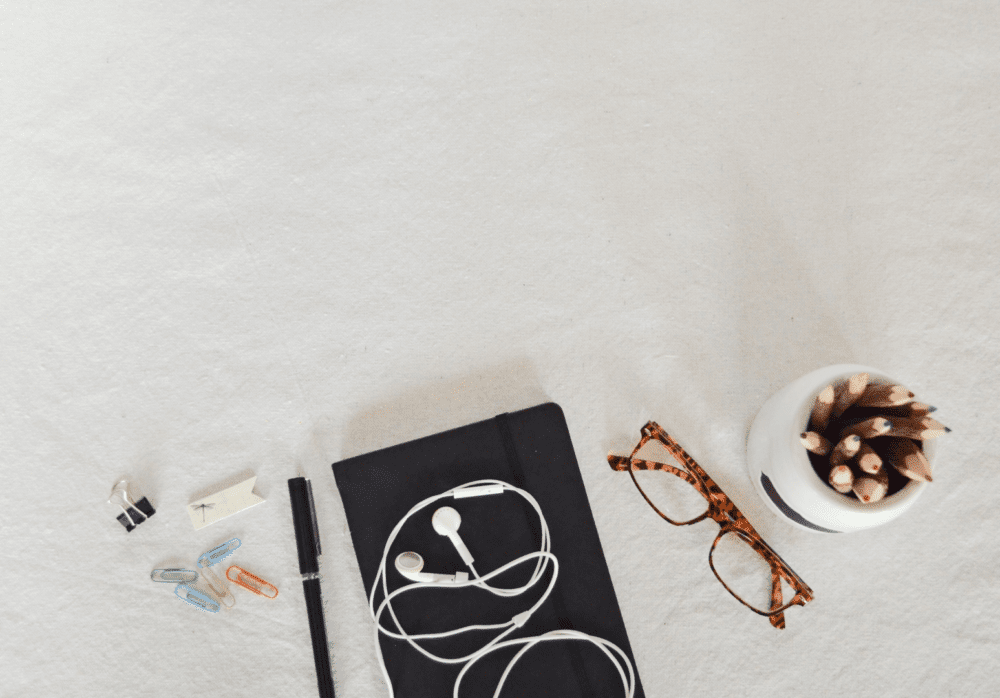 A book, a pair of glasses, some pencils, a pen, a headphone. All on a white table.