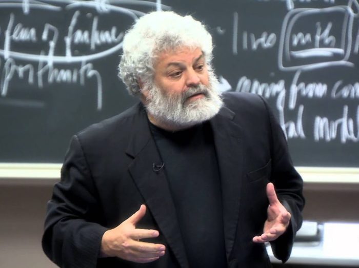 A teacher wearing black business suit stands in front of a blackboard and teaches